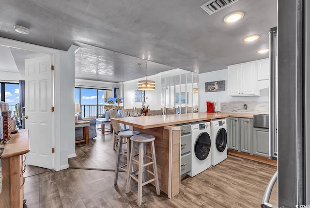 kitchen with visible vents, a peninsula, light wood-style flooring, a kitchen breakfast bar, and washing machine and dryer