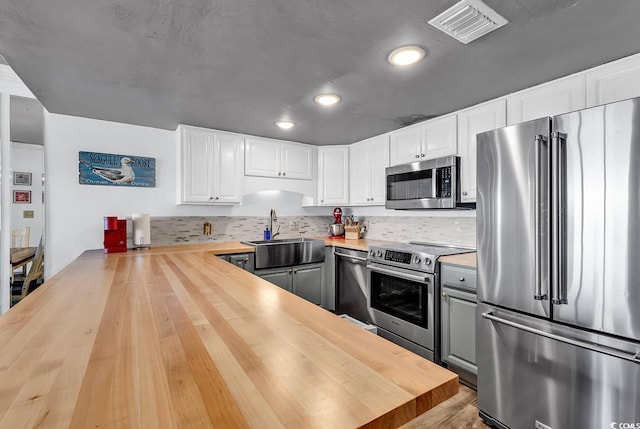 kitchen featuring visible vents, wooden counters, a sink, white cabinets, and appliances with stainless steel finishes