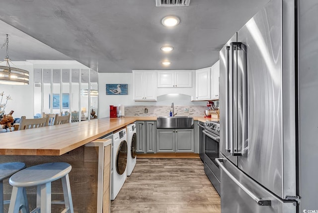 kitchen with wooden counters, a peninsula, light wood-style flooring, a sink, and appliances with stainless steel finishes