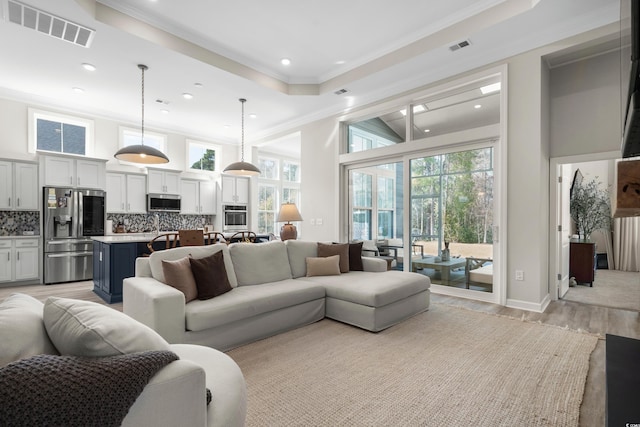 living area with light wood-type flooring, visible vents, recessed lighting, a high ceiling, and crown molding