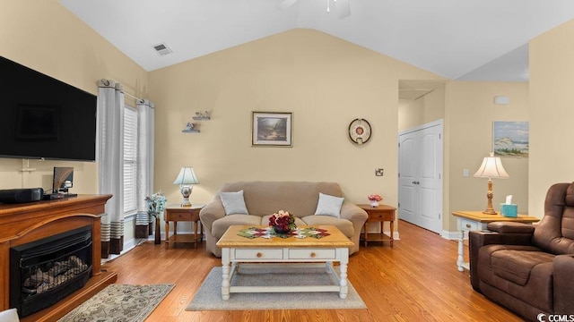 living room featuring visible vents, baseboards, light wood-type flooring, lofted ceiling, and a fireplace