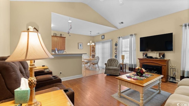 living area featuring visible vents, baseboards, lofted ceiling, a fireplace, and wood finished floors