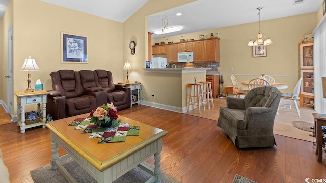 living room featuring visible vents, baseboards, vaulted ceiling, an inviting chandelier, and wood finished floors