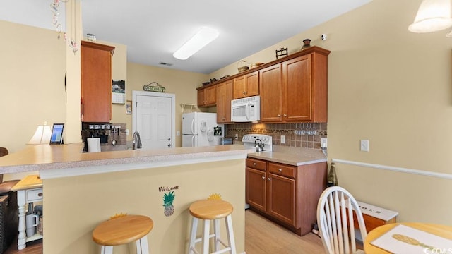 kitchen featuring decorative backsplash, white appliances, a breakfast bar area, and brown cabinetry