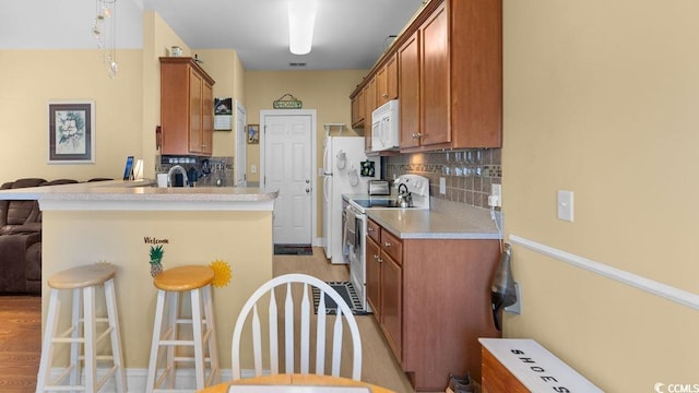 kitchen with a kitchen bar, white appliances, tasteful backsplash, and brown cabinets