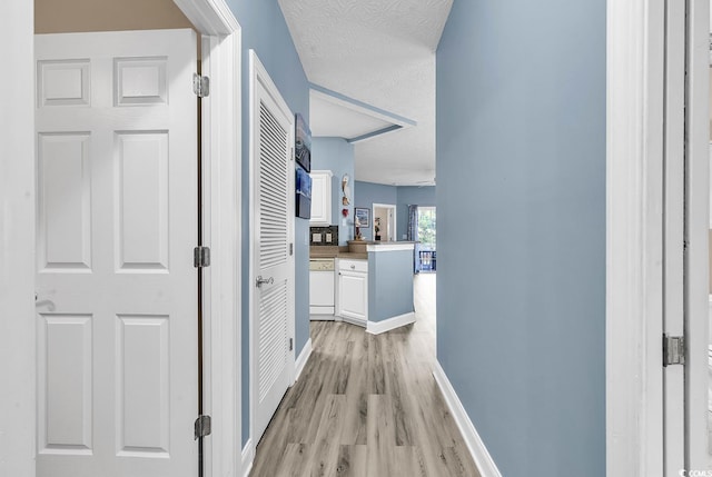 hall featuring light wood-style flooring, a textured ceiling, and baseboards