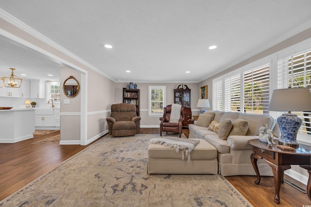 living room featuring a notable chandelier, ornamental molding, wood finished floors, recessed lighting, and baseboards