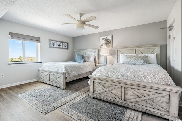 bedroom with ceiling fan, baseboards, a textured ceiling, and wood finished floors