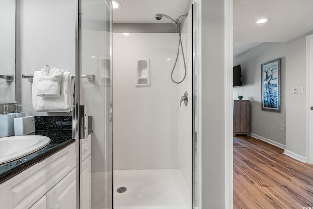 full bath featuring a stall shower, a textured ceiling, wood finished floors, baseboards, and vanity