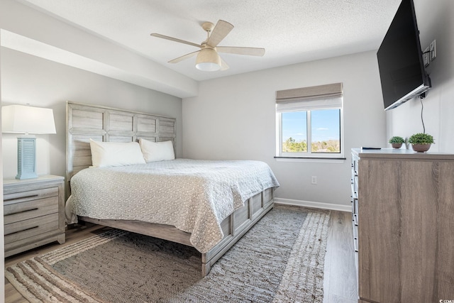 bedroom featuring light wood finished floors, a textured ceiling, baseboards, and a ceiling fan