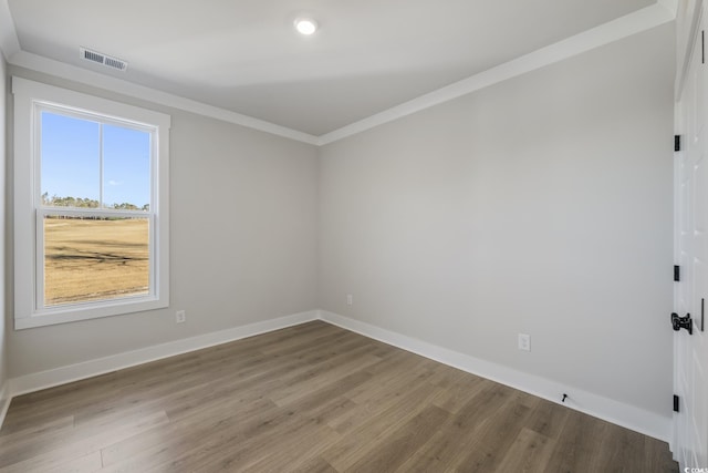 spare room with crown molding, wood finished floors, baseboards, and visible vents