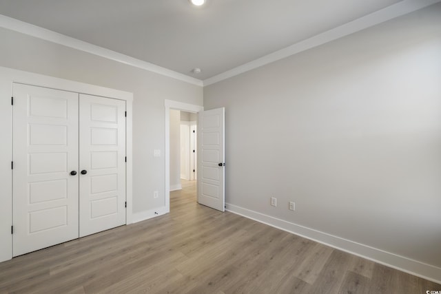 unfurnished bedroom featuring light wood finished floors, a closet, crown molding, and baseboards