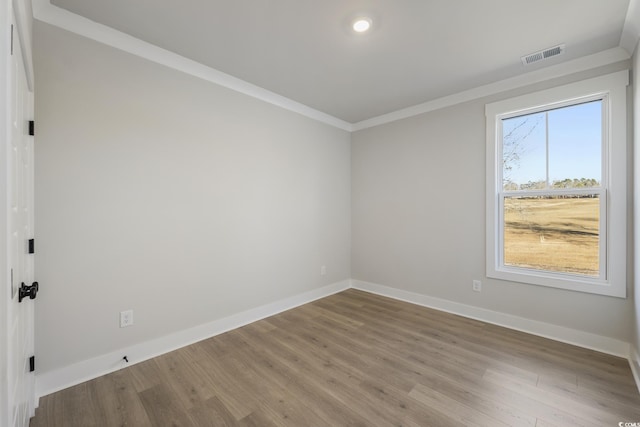 spare room with ornamental molding, wood finished floors, visible vents, and baseboards