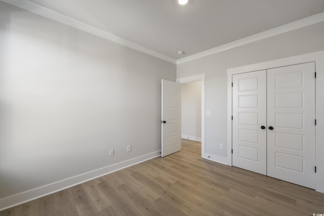 unfurnished bedroom with crown molding, wood finished floors, baseboards, and a closet