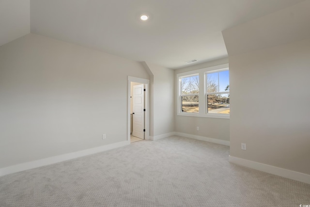 empty room with lofted ceiling, light colored carpet, visible vents, and baseboards