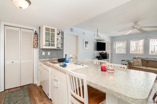 kitchen featuring a sink, light wood-style flooring, a peninsula, white dishwasher, and ceiling fan