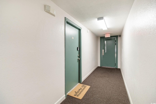 hall with baseboards, dark colored carpet, and a textured ceiling