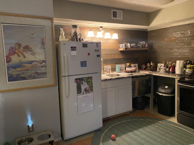 kitchen with visible vents, a sink, stainless steel range with electric cooktop, freestanding refrigerator, and wood walls