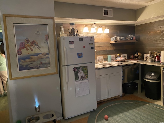 kitchen featuring visible vents, a sink, white cabinetry, freestanding refrigerator, and wood walls