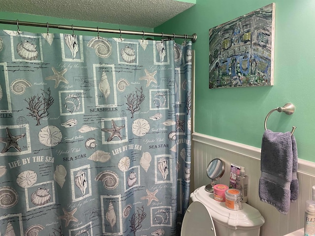 full bath with wainscoting, curtained shower, a textured ceiling, and toilet