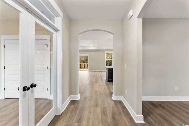 hall with arched walkways, baseboards, and wood finished floors