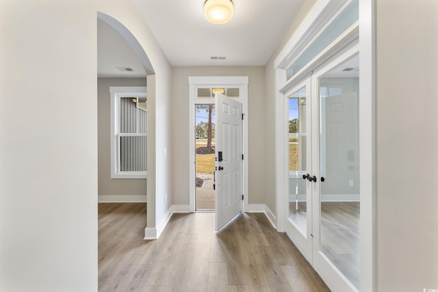 foyer entrance with visible vents, baseboards, arched walkways, and wood finished floors