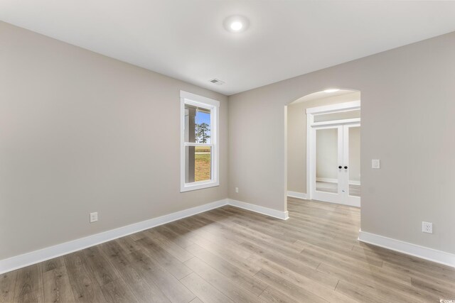 unfurnished room featuring arched walkways, visible vents, light wood-type flooring, and baseboards