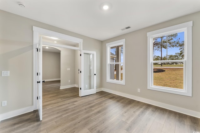 unfurnished room featuring arched walkways, visible vents, light wood-style flooring, and baseboards