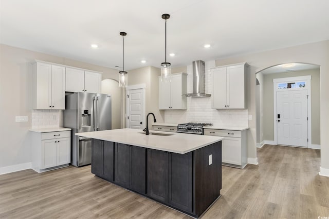 kitchen featuring a sink, stainless steel appliances, arched walkways, white cabinets, and wall chimney range hood