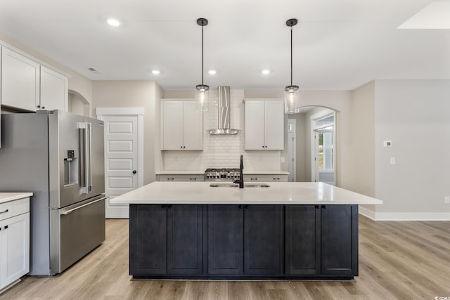 kitchen featuring arched walkways, a sink, light countertops, wall chimney exhaust hood, and high quality fridge