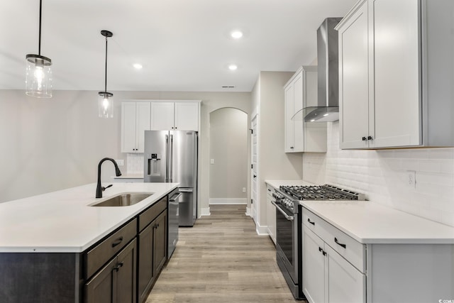 kitchen with a sink, tasteful backsplash, arched walkways, appliances with stainless steel finishes, and wall chimney range hood