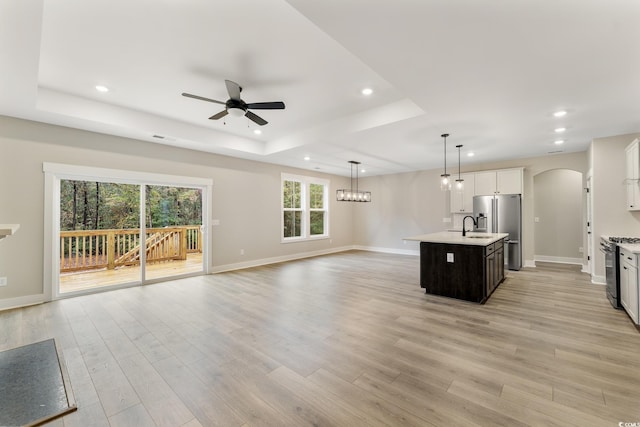 kitchen featuring arched walkways, light countertops, range with gas cooktop, a raised ceiling, and open floor plan