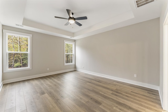 unfurnished room featuring a raised ceiling, wood finished floors, visible vents, and baseboards