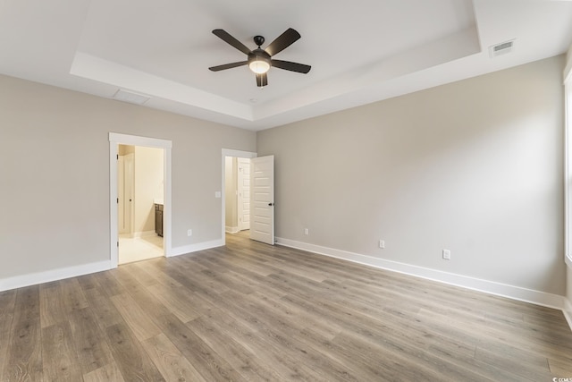 unfurnished bedroom with visible vents, baseboards, a tray ceiling, and wood finished floors