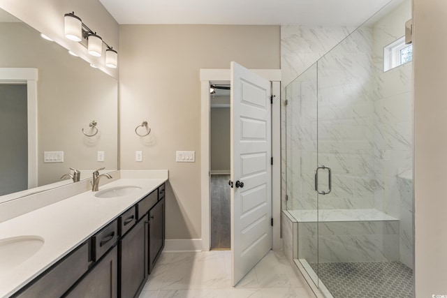 bathroom with marble finish floor, a sink, a marble finish shower, double vanity, and baseboards