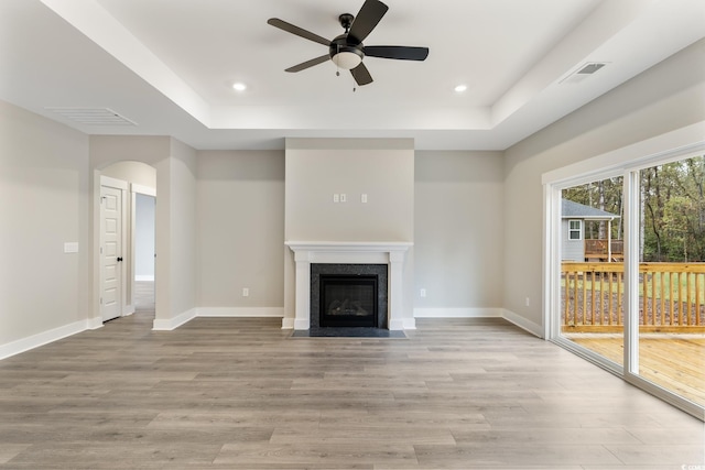 unfurnished living room with visible vents, baseboards, a fireplace with flush hearth, a raised ceiling, and light wood-type flooring