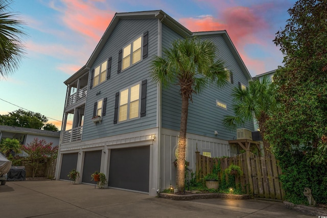 view of side of property featuring a garage, a balcony, driveway, and fence