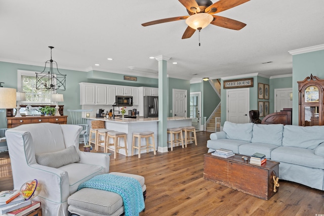 living room featuring stairway, light wood-style flooring, crown molding, and ceiling fan with notable chandelier