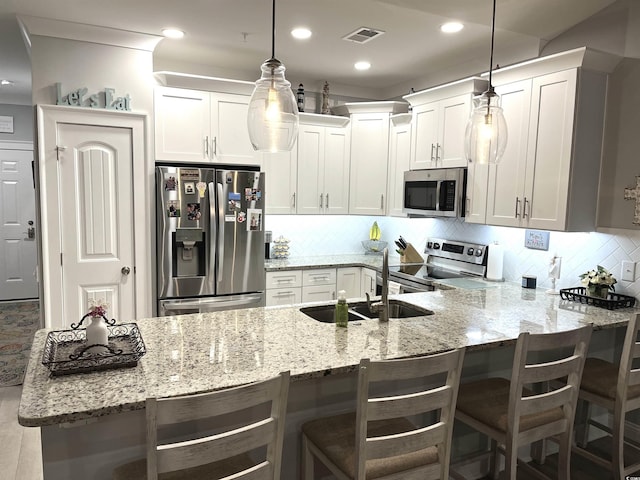 kitchen with visible vents, a sink, backsplash, appliances with stainless steel finishes, and a peninsula