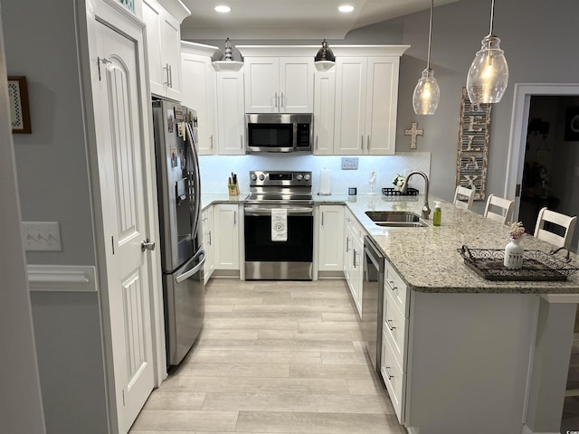 kitchen featuring a sink, tasteful backsplash, stainless steel appliances, a peninsula, and light wood finished floors