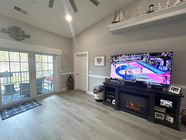 living area featuring a ceiling fan, wood finished floors, visible vents, baseboards, and lofted ceiling