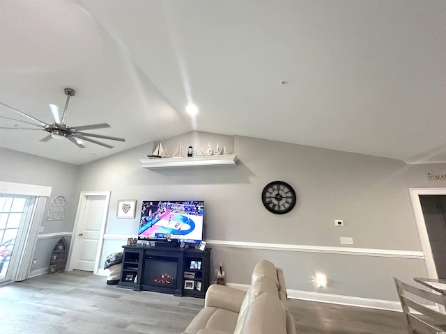 living area with a lit fireplace, a ceiling fan, lofted ceiling, and wood finished floors