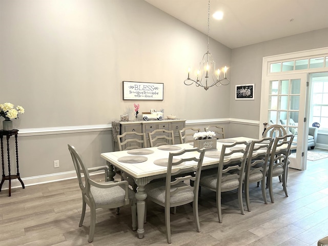 dining area featuring a wainscoted wall, a notable chandelier, light wood-style flooring, baseboards, and vaulted ceiling