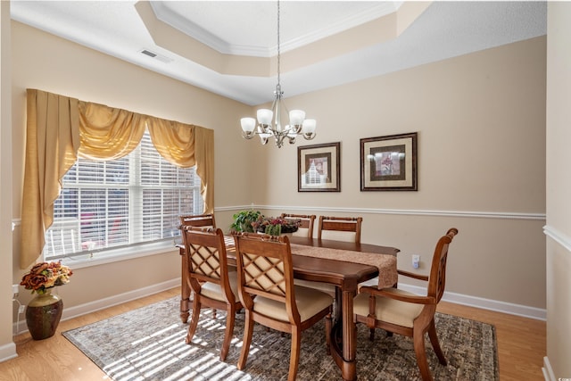 dining area featuring visible vents, a tray ceiling, wood finished floors, baseboards, and a chandelier
