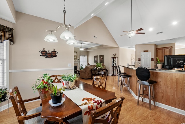 dining room with visible vents, light wood-style flooring, a fireplace, and ceiling fan