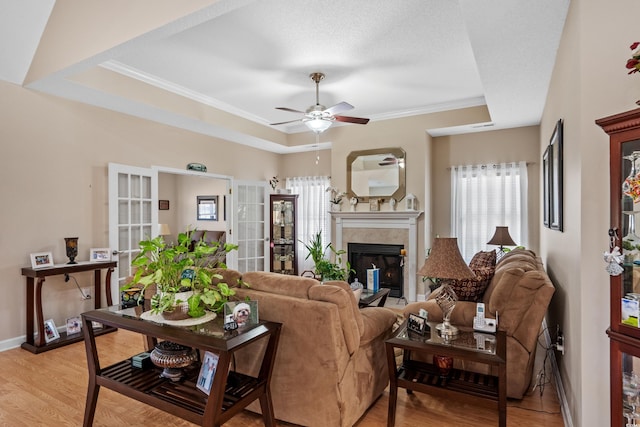 living area featuring a tiled fireplace, a tray ceiling, light wood-type flooring, and a wealth of natural light