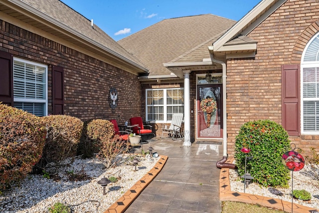 doorway to property with a patio, brick siding, and roof with shingles