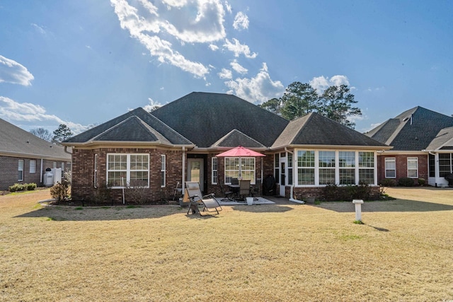 view of front of property featuring a shingled roof, a front yard, brick siding, and a patio