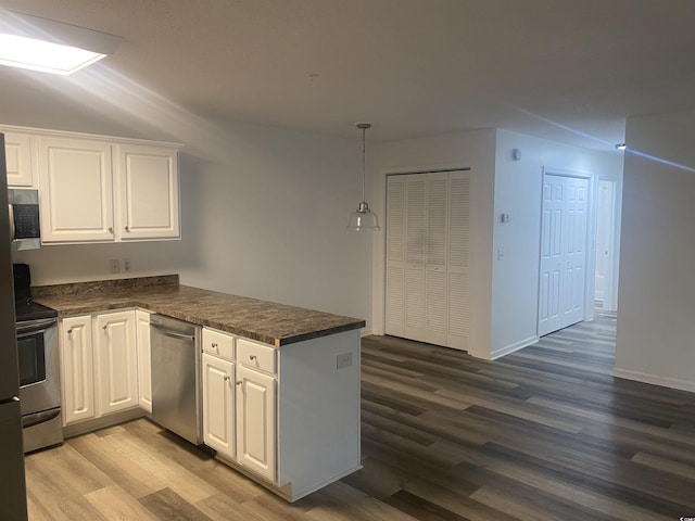 kitchen with white cabinetry, a peninsula, dark countertops, and appliances with stainless steel finishes