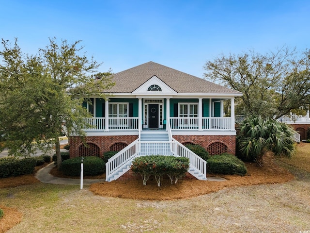 coastal inspired home with covered porch, a shingled roof, and stairs